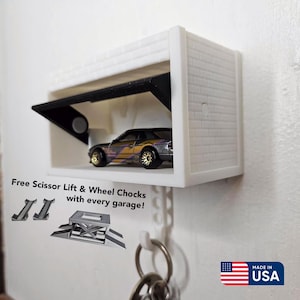 May include: A white miniature garage with a black opening door, housing a toy car with gold wheels and a purple and gold body. The garage has a brick-like texture and includes the text "Free Scissor Lift & Wheel Chocks with every garage!"