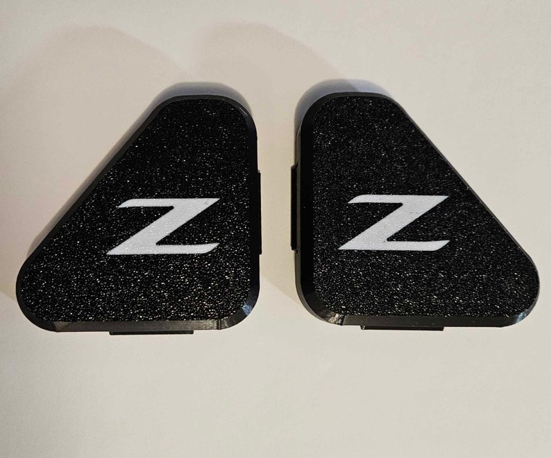 May include: Two black triangular car emblems with a white "Z" on each. The emblems have a textured surface.