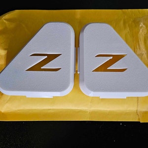 May include: Two white triangular car emblems with a gold "Z" logo on each.