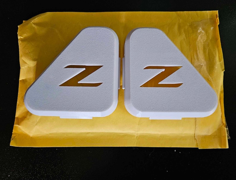 May include: Two white triangular car emblems with a gold "Z" logo on each.