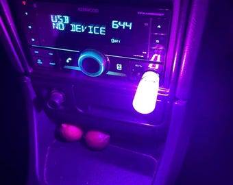 May include: A car stereo system with a USB port and a glowing USB drive. The display reads "USB NO DEVICE" and shows the time as 6:44. The interior is illuminated with a purple glow.