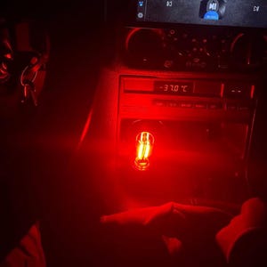 May include: Interior car shot with red lighting. A digital display shows -37.0&deg;C. A small, illuminated bulb is visible. The car's dashboard and console are in view, with keys hanging in the background.