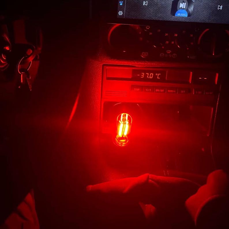 May include: Interior car shot with red lighting. A digital display shows -37.0&deg;C. A small, illuminated bulb is visible. The car's dashboard and console are in view, with keys hanging in the background.