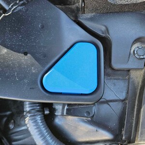 May include: A close-up of a blue plastic cap for a car's windshield washer fluid reservoir. The cap is triangular in shape and is attached to a black plastic housing.