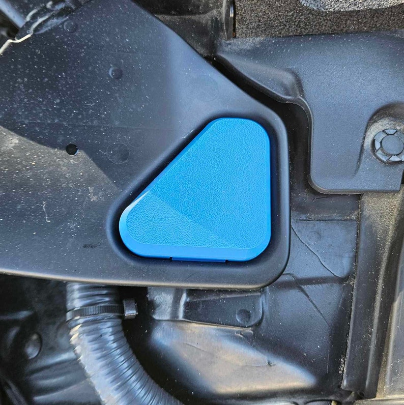 May include: A close-up of a blue plastic cap for a car's windshield washer fluid reservoir. The cap is triangular in shape and is attached to a black plastic housing.