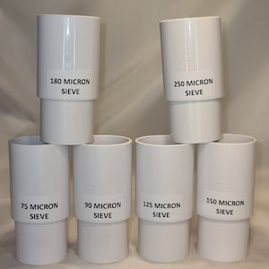 Może przedstawiać: Zbiór białych cylindrycznych sit, każde oznaczone rozmiarem w mikronach: 75, 90, 125, 150, 180 i 250. Sita ułożone są w kształt piramidy, prezentując różne rozmiary i zastosowania.