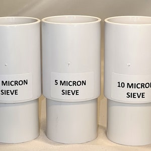 Może przedstawiać: Trzy białe plastikowe sita z etykietami wskazującymi ich rozmiar w mikronach: sito 2,5 mikrona, sito 5 mikronów i sito 10 mikronów.