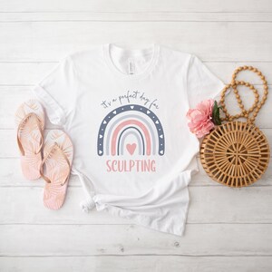 May include: White t-shirt with a rainbow design and the text "It's a perfect day for SCULPTING".
