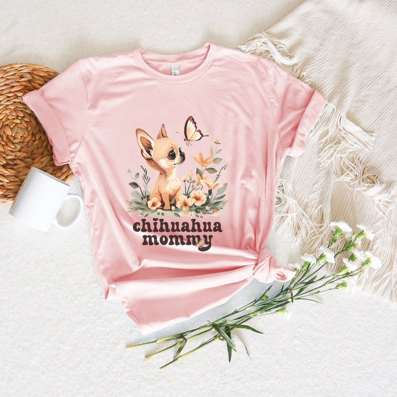 May include: Pink t-shirt with a cartoon chihuahua wearing a flower crown and a butterfly above it. The text "chihuahua mommy" is printed below the image.