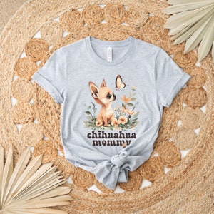 May include: A gray t-shirt with a cartoon chihuahua wearing a flower crown and a butterfly flying above it. The text "chihuahua mommy" is printed in brown letters below the image.