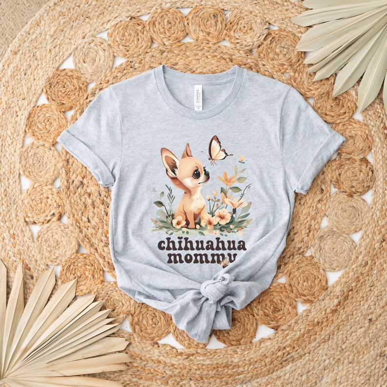 May include: A gray t-shirt with a cartoon chihuahua wearing a flower crown and a butterfly flying above it. The text "chihuahua mommy" is printed in brown letters below the image.