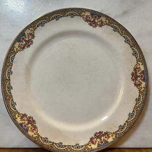 May include: A white ceramic plate with a gold rim and a floral design in shades of pink, blue, and yellow.