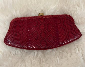 May include: A red snakeskin clutch purse with a gold clasp.