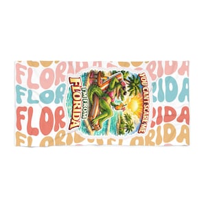 May include: A white beach towel with a repeating pattern of the word "FLORIDA" in various colors. The center features a cartoon alligator in a bikini, with the text "I'M FROM FLORIDA" and "YOU CAN'T SCARE ME".