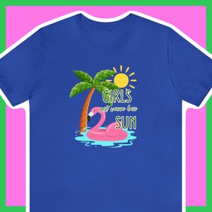 May include: A royal blue t-shirt featuring a graphic design of a pink flamingo floating on a blue pool with a palm tree and a yellow sun. The text on the shirt reads "Girls just wanna have SUN".