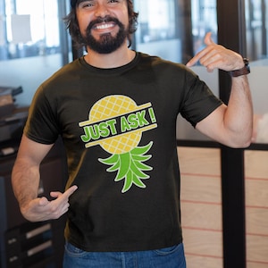 May include: A black t-shirt with a yellow pineapple graphic and the text "JUST ASK!" printed on it.