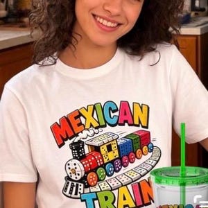 May include: A white short-sleeve t-shirt featuring a colorful graphic of a train made of dominoes with the text MEXICAN TRAIN printed in bold, multi-colored letters. The design includes a locomotive and train cars with various dot patterns.
