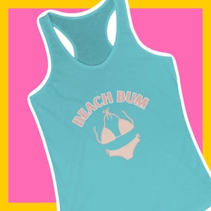 以下が含まれることがあります： ターコイズブルーのタンクトップに、ピンクの文字で「ビーチバム」と書かれています。テキストの下にはピンクのビキニが描かれています。