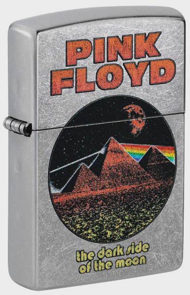 May include: Silver metal lighter featuring the Pink Floyd logo in orange lettering. The design includes a circular graphic with pyramids, a rainbow, and the words "the dark side of the moon."