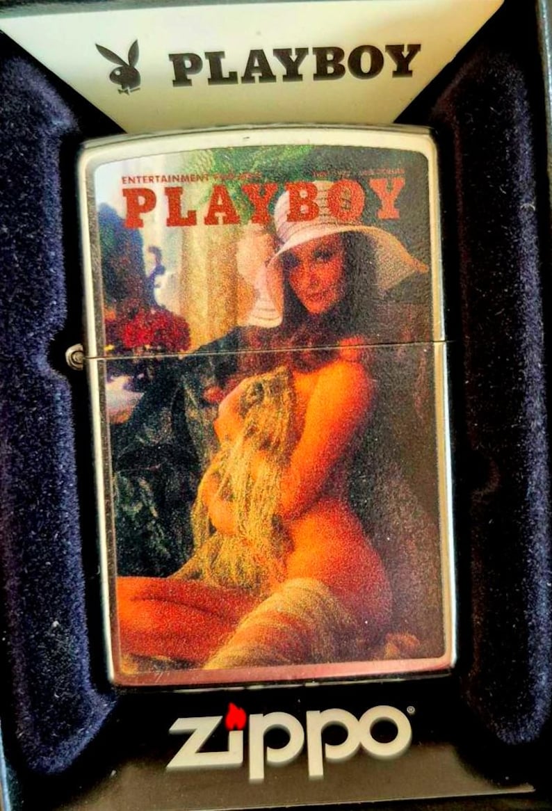 May include: A silver Zippo lighter with a vintage Playboy magazine cover. The lighter has the Playboy logo and the word "PLAYBOY" in red. The cover art shows a woman in a hat and a nude woman.