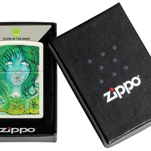 May include: A white Zippo lighter with a green and blue glow-in-the-dark design featuring a woman's face and a flower. The lighter is in a black box with the Zippo logo.