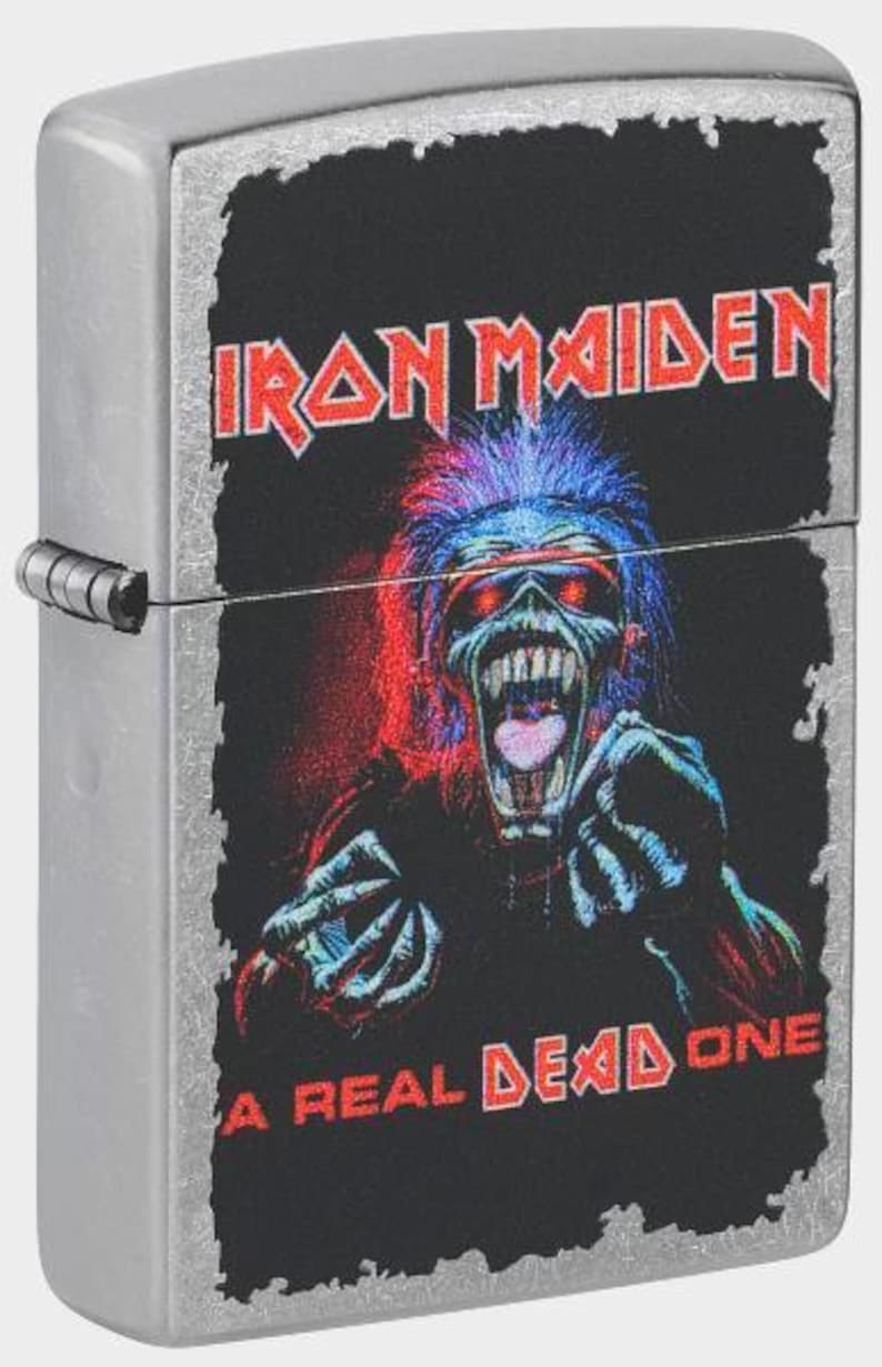 May include: A brushed chrome metal flip-top lighter featuring a graphic of the Iron Maiden mascot Eddie with red and blue highlights. The text Iron Maiden appears at the top and A Real Dead One is printed at the bottom in red lettering.
