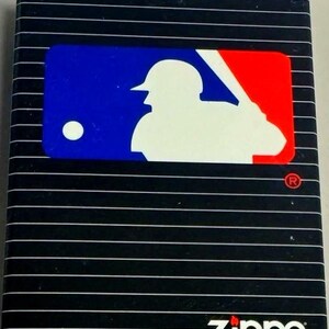 Puede incluir: Encendedor Zippo negro con tem&aacute;tica de b&eacute;isbol. El encendedor presenta el logotipo de la MLB en azul, blanco y rojo. El logotipo de Zippo es blanco. El encendedor tiene l&iacute;neas blancas horizontales. El texto "&copy; 1998 MLB, Inc." est&aacute; en la parte inferior.