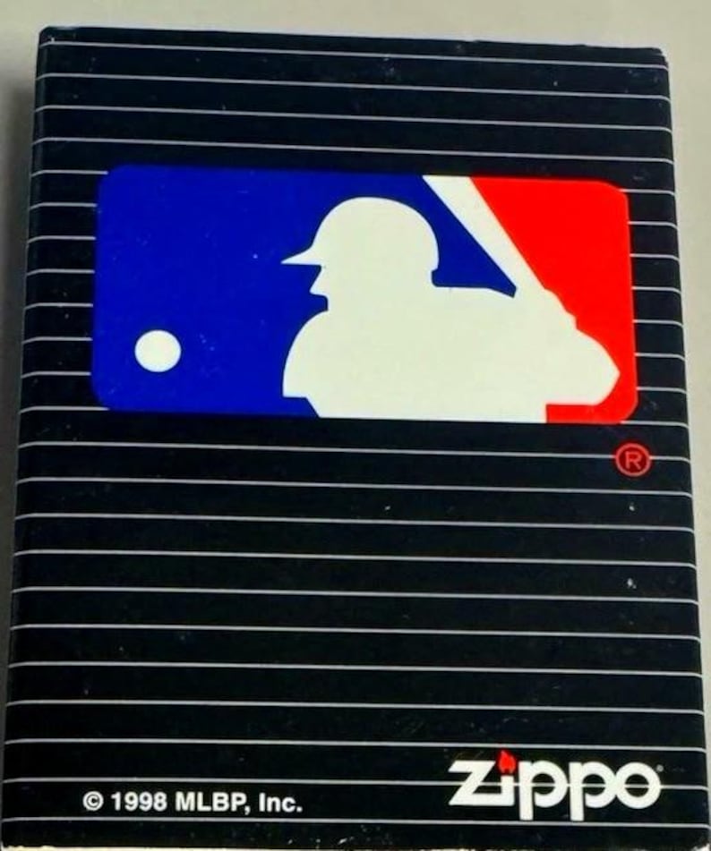 Puede incluir: Encendedor Zippo negro con tem&aacute;tica de b&eacute;isbol. El encendedor presenta el logotipo de la MLB en azul, blanco y rojo. El logotipo de Zippo es blanco. El encendedor tiene l&iacute;neas blancas horizontales. El texto "&copy; 1998 MLB, Inc." est&aacute; en la parte inferior.