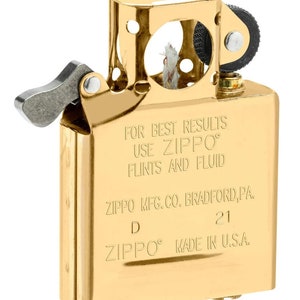 May include: A gold-colored Zippo lighter with the text "FOR BEST RESULTS USE ZIPPO FLINTS AND FLUID ZIPPO MFG.CO. BRADFORD, PA. D 21 ZIPPO MADE IN U.S.A."
