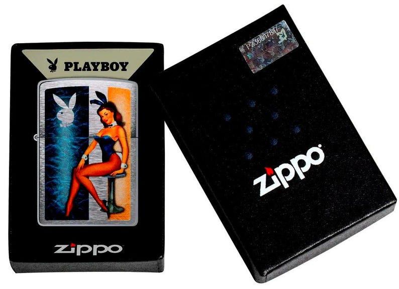 May include: A silver-tone Zippo lighter featuring a Playboy bunny graphic and a pin-up style figure in a blue bodysuit, presented in a black display box with the Zippo logo and a holographic authentication sticker on the lid.