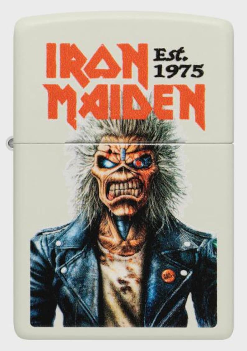 Op de afbeelding: Een cr&egrave;mekleurige aansteker met het Iron Maiden-logo in oranje en "Est. 1975" boven een illustratie van Eddie, de mascotte van de band, in een leren jas. De afbeelding is een close-up van de voorkant van de aansteker.