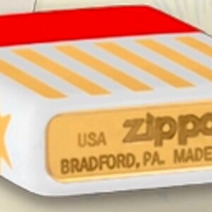 May include: A white Zippo lighter with a red top and gold star accents. The lighter features diagonal gold stripes and the Zippo logo with the text "USA BRADFORD, PA. MADE IN U.S.A."