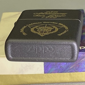 Pu&ograve; includere: Un accendino in metallo nero con scritte dorate. La parte superiore dell'accendino riporta la scritta "25th Anniversary San Diego 1996". L'accendino presenta anche la scritta "The National Cadillac Service Managers Council".