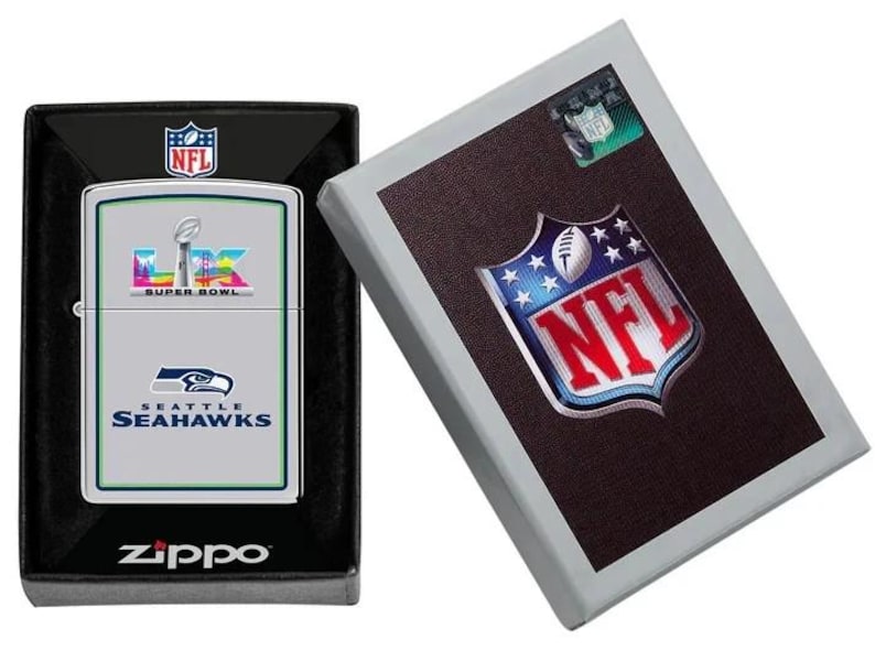 Puede incluir: Un encendedor Zippo plateado con el logotipo de los Seattle Seahawks y el texto Super Bowl LIV, presentado en una caja negra. Al lado, una caja con el logotipo de la NFL.