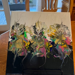 May include: Abstract painting on canvas with three colorful flowers in shades of white, black, green, yellow, pink, and gold. The flowers are set against a black background.