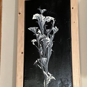 May include: A framed black and white abstract painting of a stylized flower with white paint on a black background.