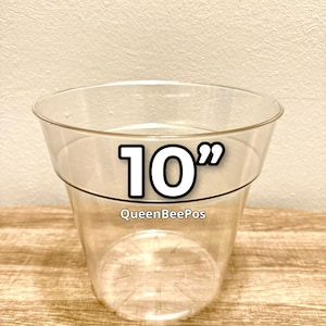 May include: A clear plastic container with a 10-inch diameter, ideal for plants or storage. The container has a wide, slightly flared rim and a transparent body. The text "QueenBeePos" is printed on the container.