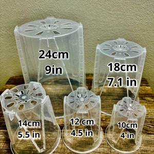 May include: Five clear plastic plant pots of different sizes. The pots are labeled with their measurements in both inches and centimeters. The largest pot is 9 inches (24 cm) tall, the next largest is 7.1 inches (18 cm) tall, followed by 5.5 inches (14 cm), 4.5 inches (12 cm), and 4 inches (10 cm).