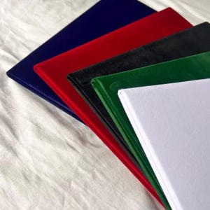 Op de afbeelding: Een stapel kleurrijke, rechthoekige stofstalen. De kleuren zijn marineblauw, rood, zwart, groen en wit. De stalen zijn in lagen gerangschikt, waarbij de randen van elke kleur zichtbaar zijn.