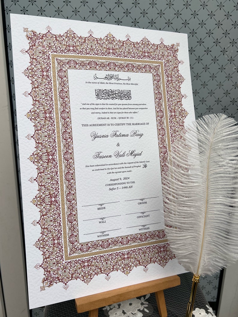 Op de afbeelding: Een huwelijkscertificaat met sierlijke bordeauxrode en gouden randdetails. Het document bevat Arabische schrift en Engelse tekst, die een huwelijk bevestigt. Een witte veren pen ligt in de buurt, wat duidt op een formele gelegenheid.