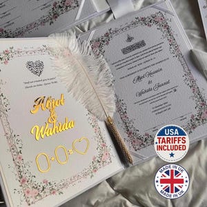 Puede incluir: Juego de invitaciones de boda con detalles florales y dorados. La invitación abierta muestra los nombres "Aojol & Wahida" en letras doradas, con un símbolo de corazón. Una pluma blanca descansa sobre la invitación.