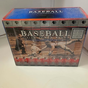 Könnte beinhalten: Eine Box-Set der PBS Home Video-Serie "Baseball: A Film by Ken Burns". Die blaue Box zeigt Bilder von Baseballspielern und den Titel in großen weißen Buchstaben. Das Set enthält mehrere VHS-Kassetten.