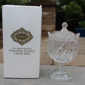Könnte beinhalten: Eine transparente Bleikristall-Bonbonniere mit einem ananasfüßigen Sockel und einem Deckel. Die Box befindet sich neben ihrer weißen Box mit dem Text "24% Lead Crystal Pineapple Footed Candy Box".