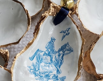 May include: A set of oyster shell ornaments with gold trim. One ornament features a blue and white illustration of a rider on horseback with a bird flying overhead.