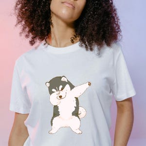 Puede incluir: Camiseta blanca con una ilustración de dibujos animados de un perro blanco y negro haciendo el dab.