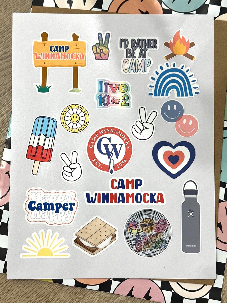 May include: A collection of colorful stickers featuring camp-themed designs, including a peace sign, a campfire, a rainbow, a smiley face, a popsicle, a heart, a sun, a s'more, a water bottle, and a sign that reads "Camp Winnamocka".
