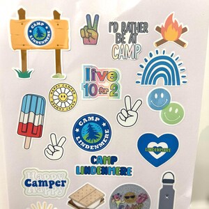 May include: A collection of colorful stickers featuring camp-themed designs, including a peace sign, a campfire, a rainbow, a smiley face, a popsicle, a heart, a sign that says "Camp Lindenmere", and a s'more.