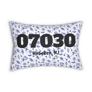 Può includere: Cuscino rettangolare con sfondo bianco e motivo floreale blu. Il cuscino presenta i numeri neri "07030" e il testo "Hoboken, NJ". Un accessorio decorativo per la casa.