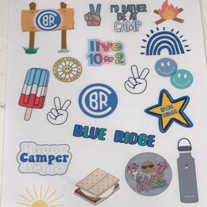 May include: A sheet of colorful stickers with a camp theme. The stickers feature a variety of designs, including a campfire, a rainbow, a peace sign, a popsicle, a s'more, a water bottle, and a star with the words "Blue Ridge" on it. The stickers also feature the letters "BR" in a circle, the words "Happy Camper", and the words "I'd rather be at camp".