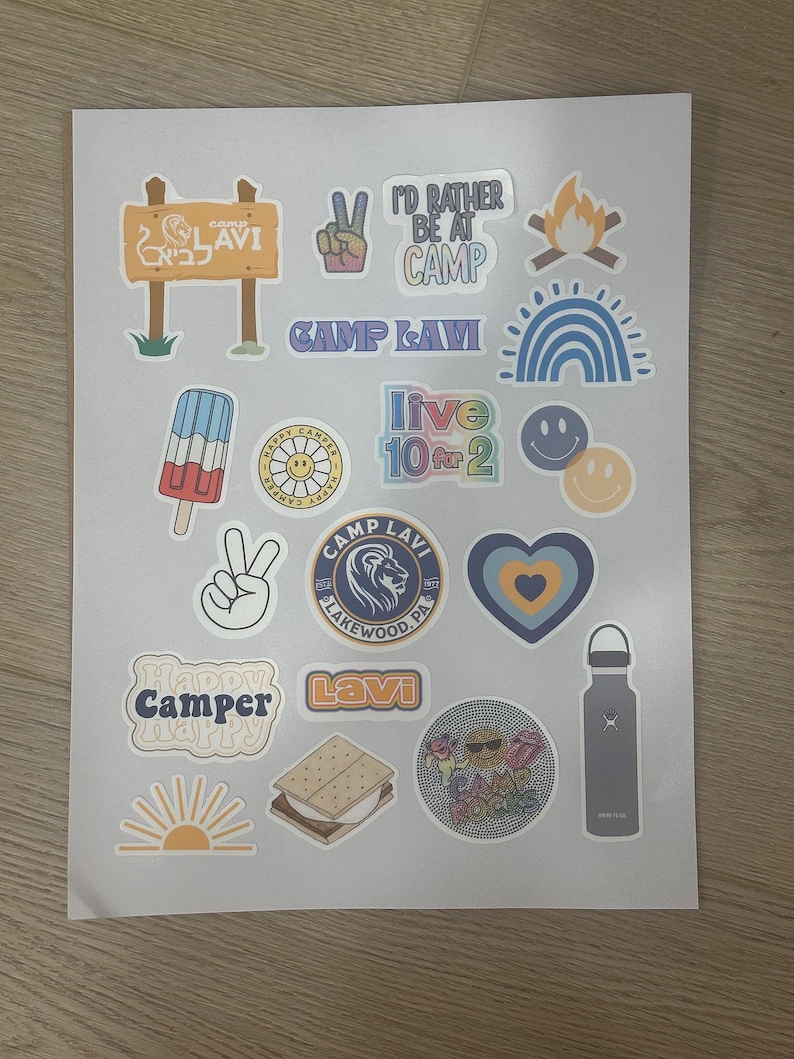 May include: A collection of colorful stickers featuring camp-themed designs, including a peace sign, a campfire, a rainbow, a popsicle, a smiley face, a heart, a sun, a s'more, a water bottle, and a lion logo with the text "Camp Lavi Lakewood, PA".